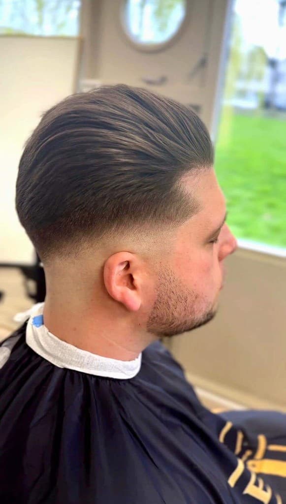 Strakke high skin fade met slick back op kruin, profiel in de salon met daglicht